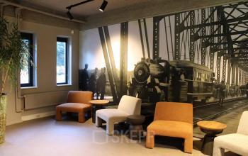 Office lounge area with brown and grey seating at Keulenstraat 12 in Deventer, featuring a large mural of a train on the wall.