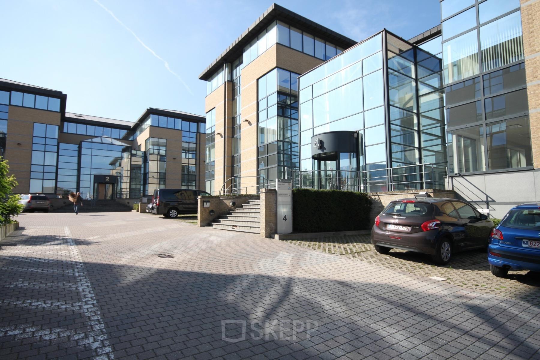 Exterior view of office building at Pontbeekstraat 2-4, Dilbeek, with large glass windows and parking space.