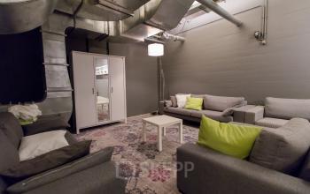 Cozy office lounge with gray sofas, a coffee table, and industrial ceiling pipes at Berglaan 4-8, Drachten.