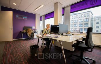 Modern office space with large windows at Berglaan 4-8, Drachten, featuring workstations, chairs, and a business professional working at a desk.