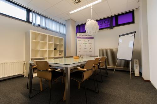 Conference room with glass table, six chairs, shelving unit, whiteboard, and promotional poster at Berglaan 4-8, Drachten.
