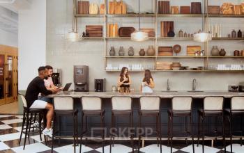 Ein moderner Büroraum in der Grünstraße 15, Düsseldorf Altstadt, mit Personen, die Gespräche führen und Laptops an einer stilvollen Bar nutzen. Perfekt, um ein Büro zu mieten.