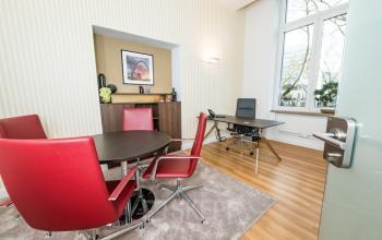 Moderner Büroraum mit Holzboden an der Königsallee 27, Düsseldorf Altstadt. Roter Konferenztisch mit Stühlen und Arbeitsstation. Gelegenheit zur Bürofläche mieten.