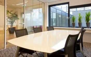 Modern conference room at Galvanistraat 1, Ede, featuring a sleek white table, black chairs, large windows with plants, and glass walls.