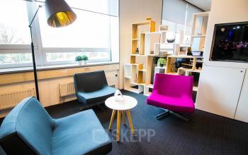 Cozy office space available for rent at Eindhoven Airport featuring stylish seating, a small table, and natural light. Ideal for relaxed meetings.