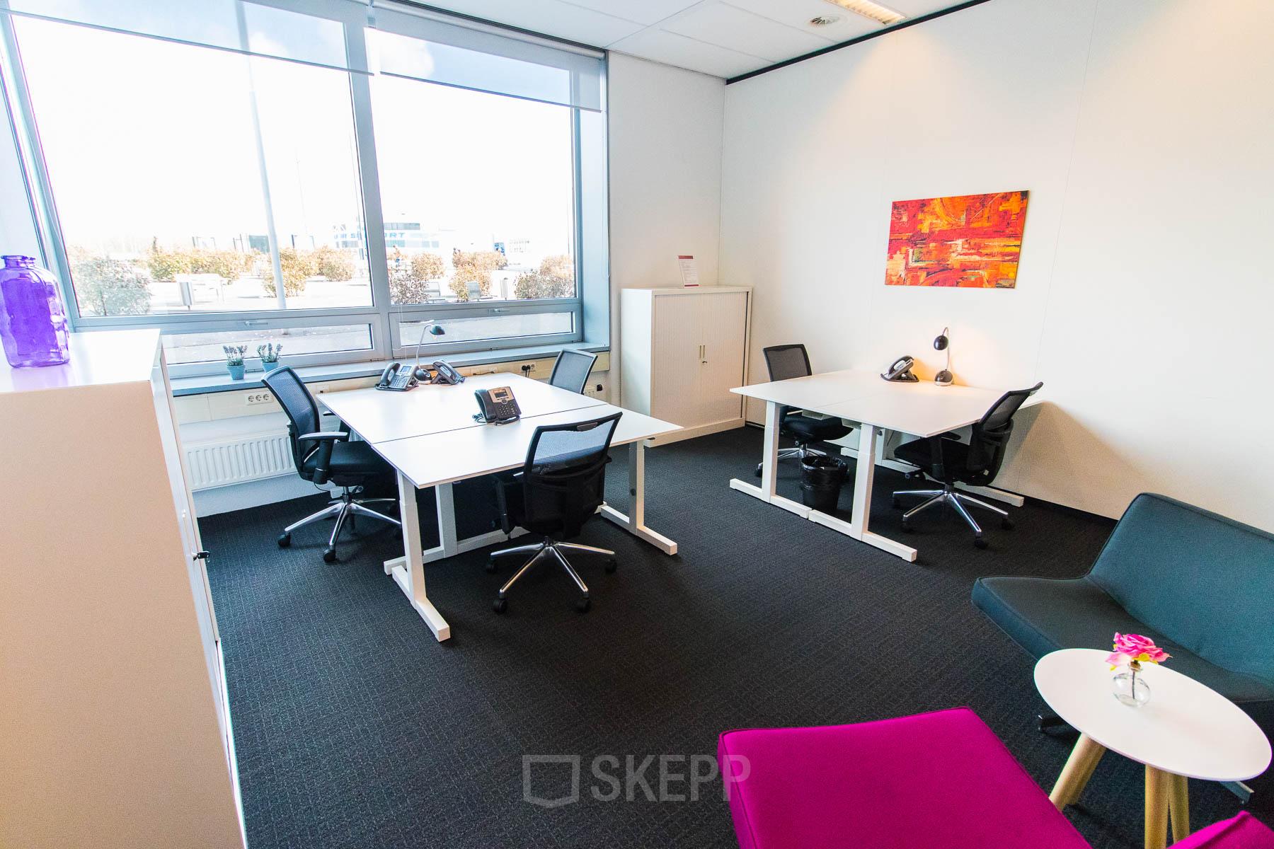 A bright office space for rent at Eindhoven Airport with four desks, ergonomic chairs, and a colorful wall art, offering a functional workspace for productivity.