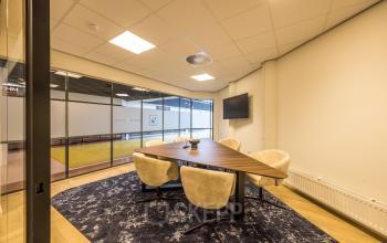 Modern office space at Luchthavenweg 81, fitted for meetings with a sleek table, beige chairs, and a wall-mounted screen available for rent at Eindhoven Airport.