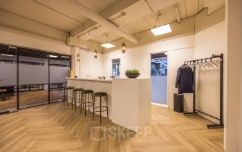 Stylish office space for rent at Luchthavenweg 81, Eindhoven Airport featuring a modern bar area with stools, warm lighting, and a nearby coat rack.