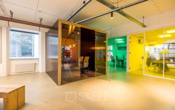 Modern office space rental at Eindhoven Airport with a unique cube structure, offering an open floorplan and brightly colored rooms surrounding a central workspace.