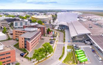 Aerial view of office building located at Luchthavenweg 55 in Eindhoven Airport, Eindhoven, surrounded by other buildings and roads. Ideal office space rental location near the airport.