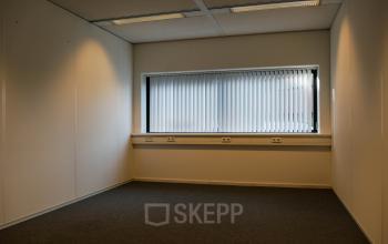 Compact office space available for rent at Luchthavenweg 55, Eindhoven Airport with carpeted floors and a window with vertical blinds.