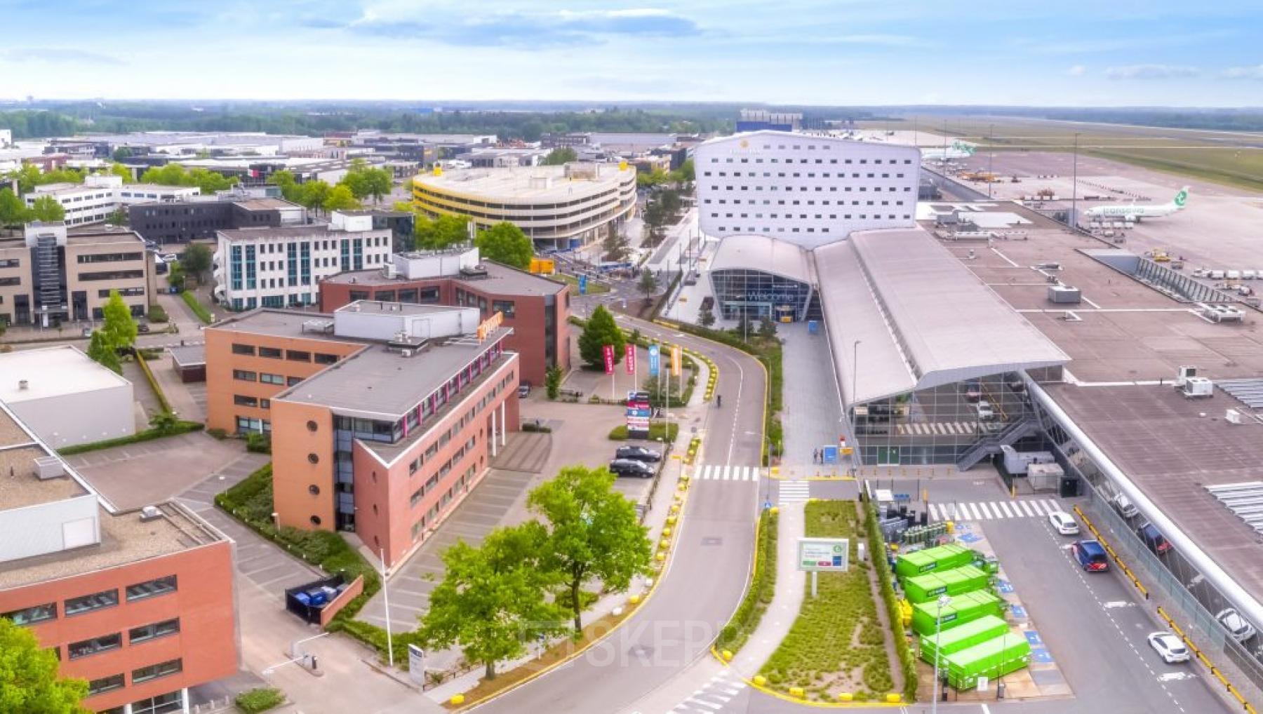 Aerial view of office building located at Luchthavenweg 55 in Eindhoven Airport, Eindhoven, surrounded by other buildings and roads. Ideal office space rental location near the airport.