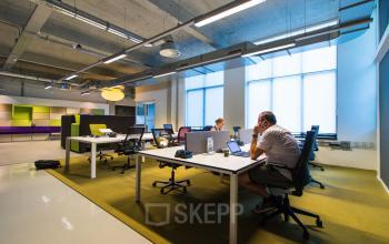Modern office space for rent at Lichttoren 32 in Eindhoven Center, with people working at desks and vibrant decor.