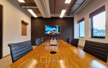 Contemporary conference room with a wooden table and black leather chairs, featuring a large TV on the wall in an office space rental at Emmasingel 33, Eindhoven Center.