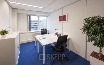 Modern office space rental at Fellenoord 130, Eindhoven Center, with a well-lit desk, comfortable chair, and vibrant blue carpet.