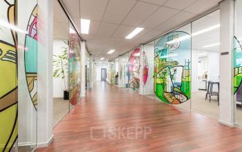 Vibrant office space at Meerenakkerplein 11-20, Eindhoven De Hurk, featuring colorful stained glass partitions and wooden floors. Ideal for office space rental.