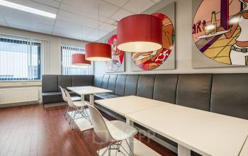 Modern office space in Eindhoven De Hurk featuring artistic wall decor, sleek tables, and contemporary pendant lighting, available for office space rental.