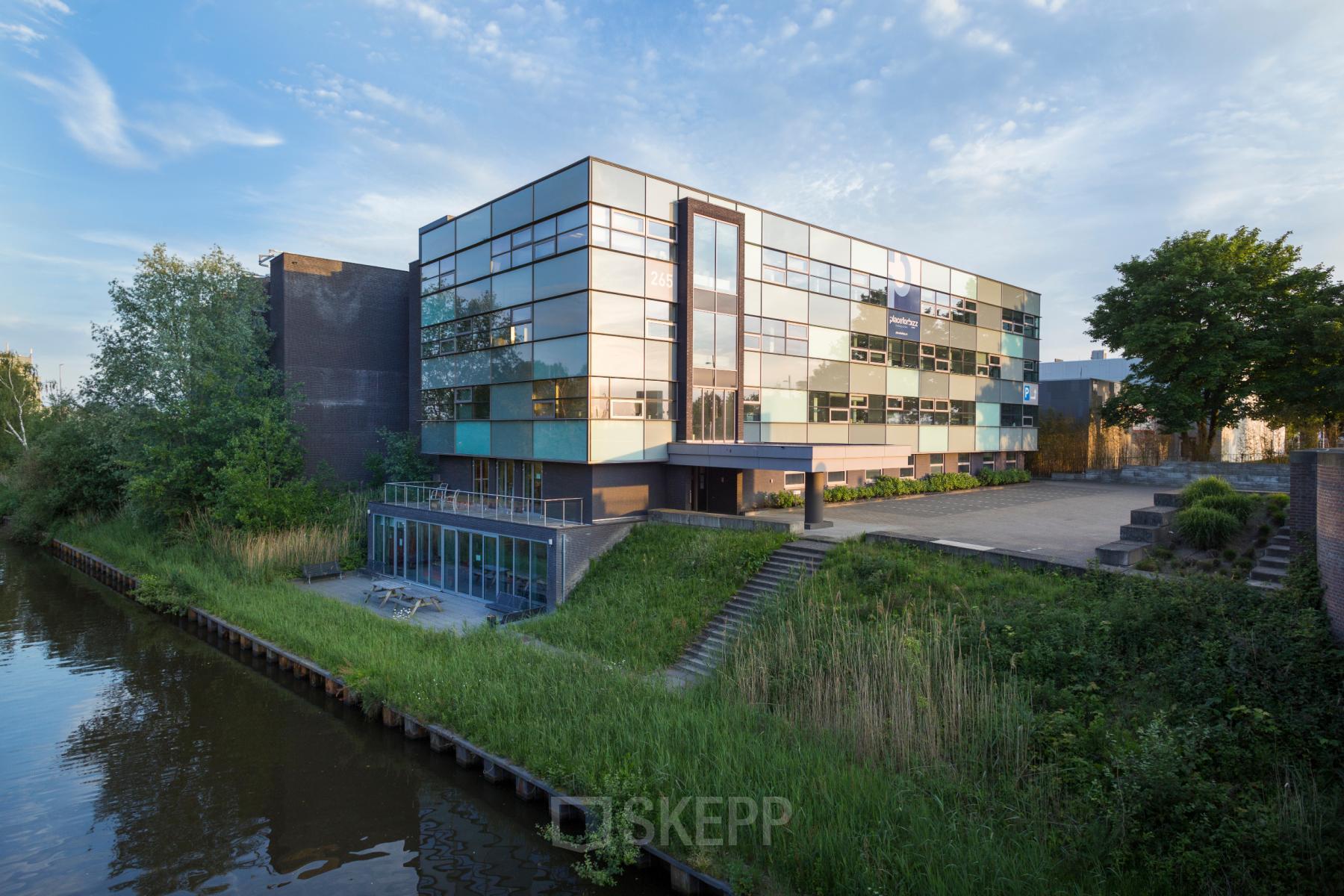 Exterior view of modern office building located at Hurksestraat 60, Eindhoven De Hurk, featuring glass windows and canal-side setting.