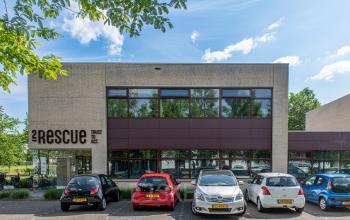 Exterior view of office building at Le Havre 114-127, Eindhoven North, featuring modern architecture and a parking area with several parked cars.