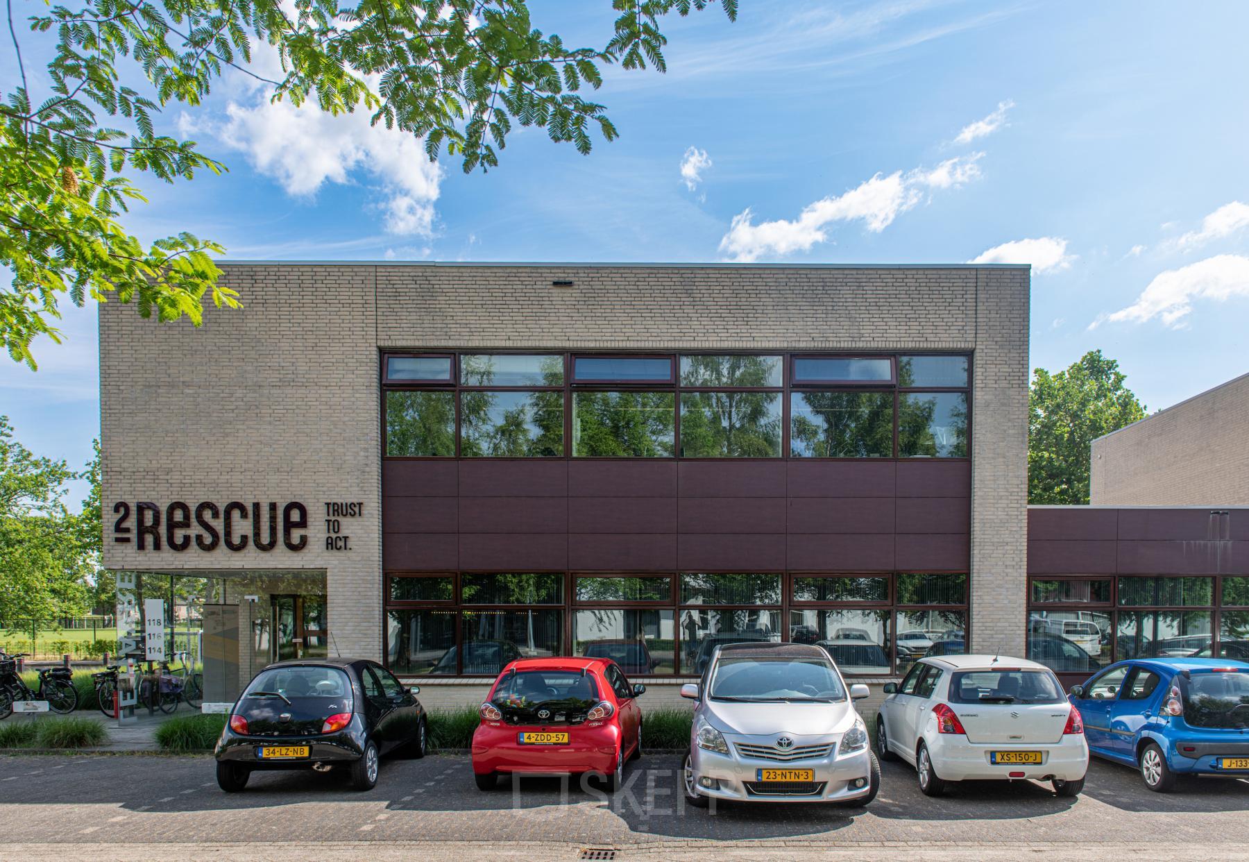 Exterior view of office building at Le Havre 114-127, Eindhoven North, featuring modern architecture and a parking area with several parked cars.