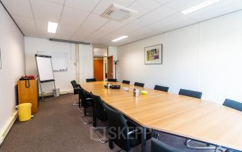 A conference room at Weegschaalstraat 3, Eindhoven North, featuring a long table with black chairs, a whiteboard, and a flip chart, ideal for office space rental.