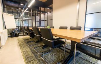 Spacious conference room available for office space rental at Weegschaalstraat 3, Eindhoven North, featuring a long wooden table with black chairs and a glass partition wall.