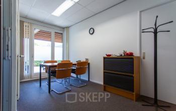 Compact office space rental at Weegschaalstraat 3, Eindhoven North, featuring a table with chairs, storage cabinet, and natural light from large windows.
