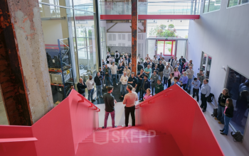 Bright, bustling entrance at Frederiklaan 10A, Eindhoven Strijp-S, featuring a vibrant red staircase and a crowd engaged in a lively business networking event. Ideal office space rental for dynamic professionals.