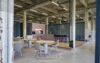 Spacious and modern office interior at Frederiklaan 10A, Eindhoven Strijp-S, featuring a contemporary open floor plan with stylish tables, chairs, and a sleek kitchen area, ideal for office space rental.