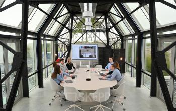Modern conference room in Eindhoven Strijp-S at Frederiklaan 10A, featuring a glass-walled space with a large table surrounded by professionals engaged in business discussions. Ideal for office space rental.