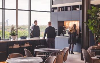 Modern furnished office space at Achtseweg Zuid 159R, Eindhoven Strijp-S, featuring people engaging in conversation by a coffee station.