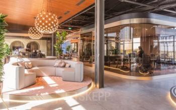 Modern office space in Eindhoven Strijp-S with stylish seating and a meeting room. Ideal for office space rental, highlighted by unique lighting and contemporary decor.