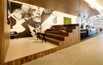 Contemporary office space at Frederiklaan 10E, Eindhoven Strijp-S, featuring wooden tiered seating with cushions and a stylish wall mural, available for office space rental.