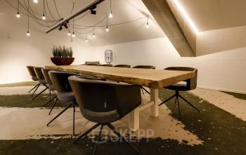Spacious office conference room with a large wooden table, surrounded by modern chairs and ambient lighting, perfect for office space rental at Frederiklaan 10E, Eindhoven Strijp-S.