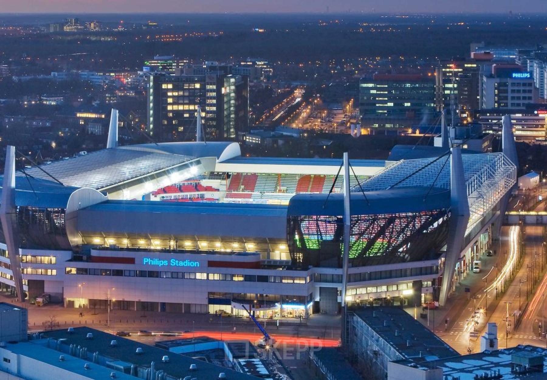 An evening aerial view of the Philips Stadium in Eindhoven, showcasing the surrounding city lights and structures.