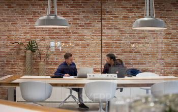 Two people engaged in discussion at a modern, furnished workspace with exposed brick walls in Eindhoven Strijp-S. Ideal for office space rental seekers.