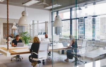 Office space rental at Torenallee 20, Eindhoven Strijp-S, featuring a modern interior with glass walls and people engaged in business activities at desks.
