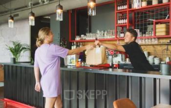 Two people interact at a modern bar area within an office at Torenallee 20, Eindhoven Strijp-S, showcasing opportunities for office space rental.