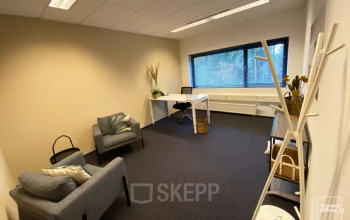 Furnished office to rent at Boermarkeweg 58a, Emmen, featuring a desk, chair, and seating area with natural light from a large window.