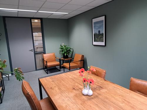 Modern office space with wooden table, leather chairs, and green walls at Hoenderkamp 20, Emmen, ideal for rent. Features a framed landscape photo and indoor plants, creating a cozy work environment.