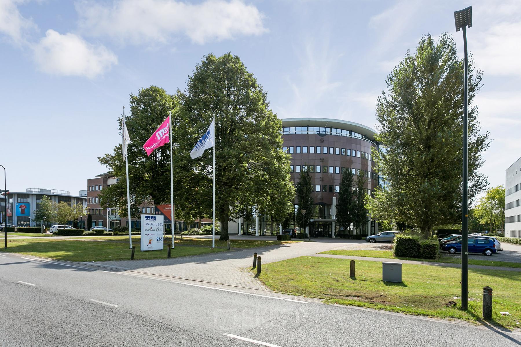Exterior view of an office building located at Hengelosestraat 581, Enschede, with flags, trees, and parking facilities visible.