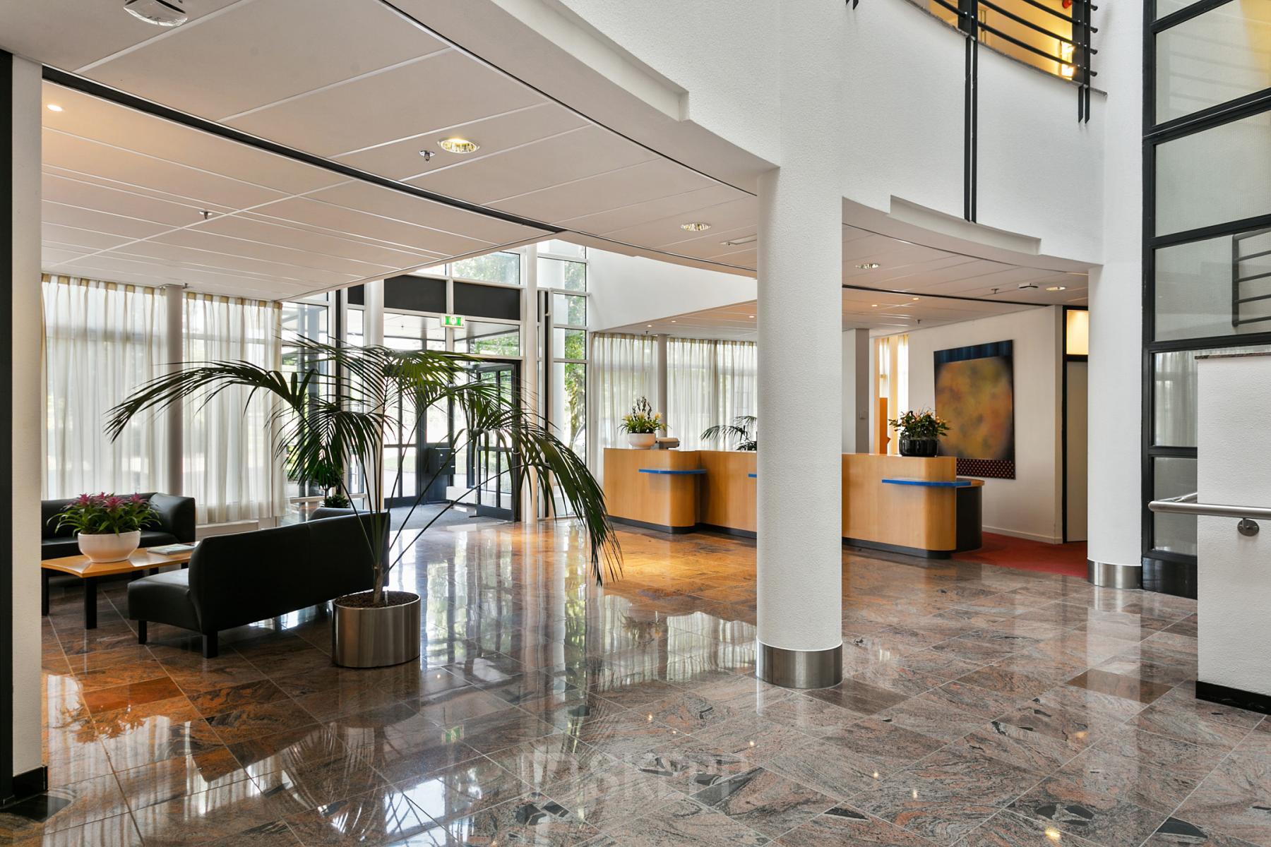 Modern lobby area of an office building at Hengelosestraat 581, Enschede with marble floors, reception desks, and seating area.