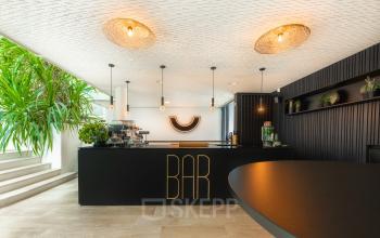 Modern office interior at Brouwerijstraat 1, Enschede, featuring a stylish bar area with sleek black design and ambient lighting, perfect for socializing. Suitable for an office space rental.