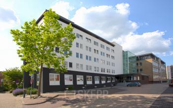 Exterior view of a modern office building, located at Brouwerijstraat 1, Enschede, featuring a clean white facade with black accents and large windows. Ideal for office space rental with ample light and contemporary design.