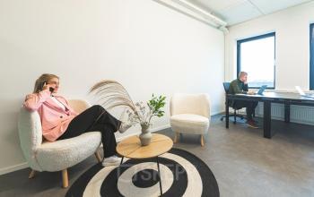 Modern office space at Brouwerijstraat 1, Enschede featuring a light interior with contemporary furniture, two professionals working. Ideal for office space rental.