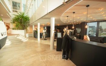 Reception area at Brouwerijstraat 1 in Enschede with people working at the front desk and open space with plants and modern lighting.