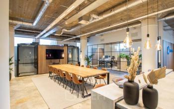 Modern open floorplan office space at Brouwerijstraat 1 in Enschede with a large wooden conference table and glass-walled meeting rooms.