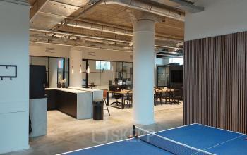 Modern office space at Brouwerijstraat 1, Enschede, featuring open workspaces with a ping pong table, sleek furniture, and industrial ceiling. Ideal for office space rental needs.