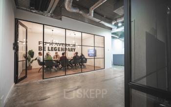 Modern conference room at Brouwerijstraat 1, Enschede, with glass walls and ceiling lighting, featuring a team having a meeting around a table.