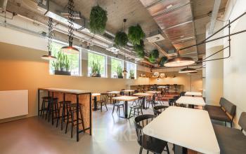 Modern office space rental at Brouwerijstraat 1, Enschede featuring a stylish interior with tables, chairs, and hanging planters.